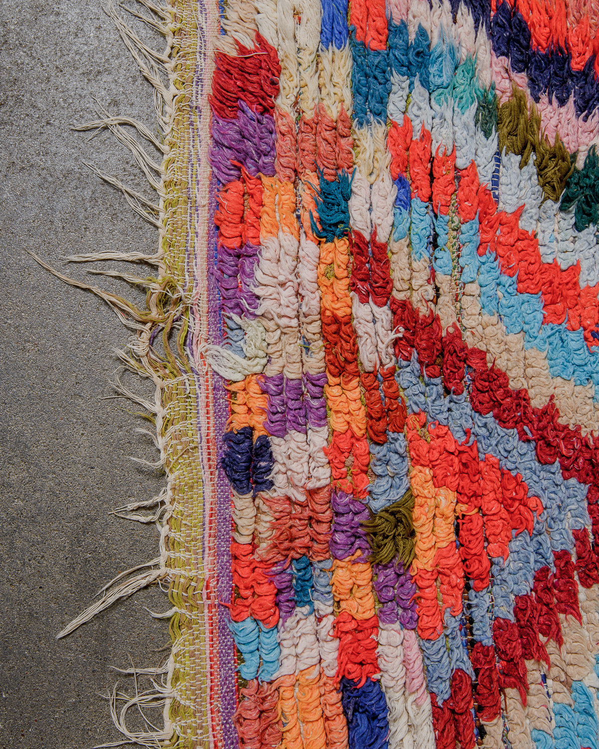 Multicoloured textured rug with fringes and hole at end on a concrete floor